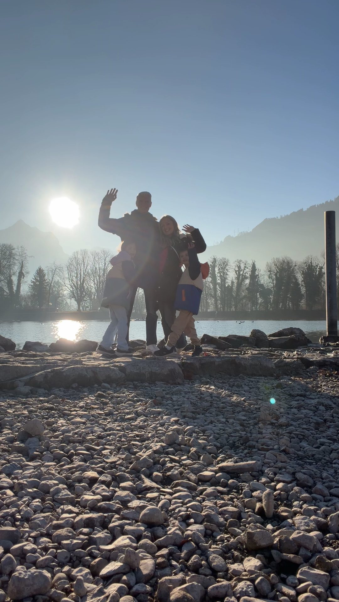 A family waving by a lake in the winter sun